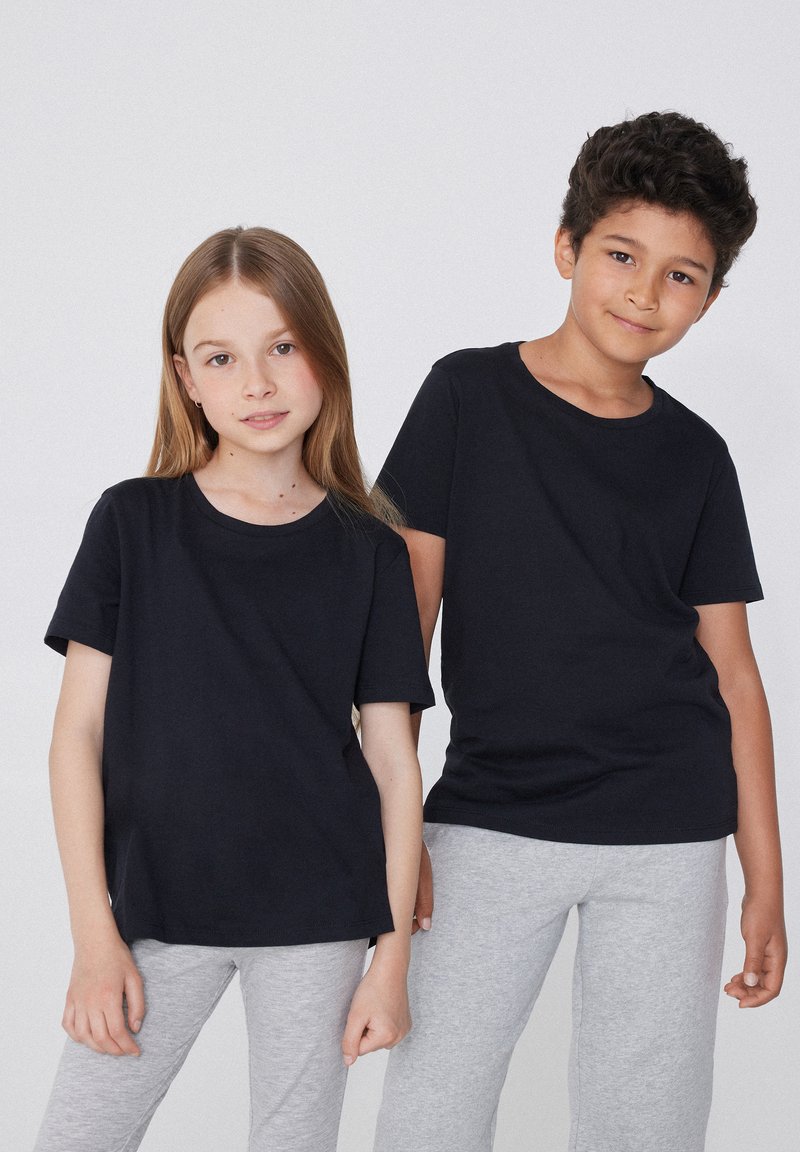 Černé bavlněné trička s kulatým výstřihem, krátkým rukávem a volným střihem, spojené se šedými sportovními kalhotami.