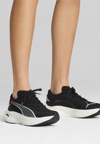 Zapatillas deportivas negras con parte superior de malla, con acentos blancos y una suela texturizada. Los cordones son negros; el logotipo es visible en el lateral.
