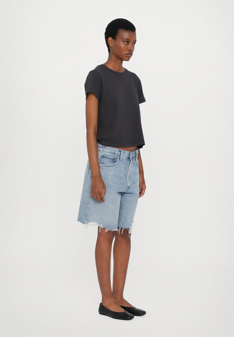 Cropped black short-sleeve T-shirt, light blue denim shorts with frayed hem, and flat black shoes. Simple and casual design.