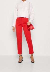 Chemise blanche à col, courte, en tissu de coton, associée à un pantalon taille haute rouge vif. Accessoirisée avec un petit sac en satin rouge.