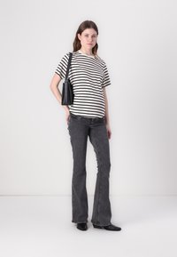 Tricou cu dungi alb-negru, croială lejeră, asortat cu blugi negri închiși, evazați. Modelul poartă o geantă mică de umăr neagră, stând pe un fundal alb.