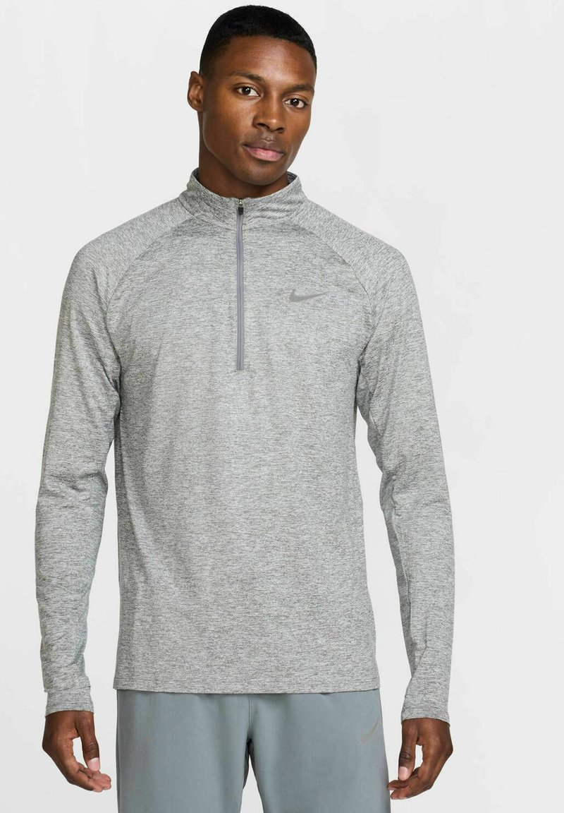 Maglia atletica grigia a maniche lunghe con zip a metà, realizzata in un tessuto traspirante. Presenta maniche raglan e un logo discreto sul petto.