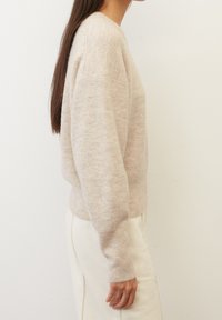 Suéter de punto de color beige claro con textura acanalada y mangas largas. Cuello redondo y corte relajado, combinado con pantalones de color crema.