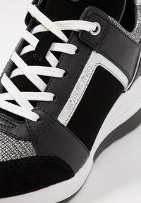 Baskets Michael Kors en noir et blanc avec lacets blancs, panneaux en cuir et en daim, et tissu argenté texturé près de la zone des orteils.