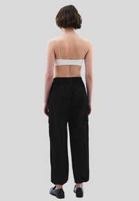 Černé cargo kalhoty s elastickým pasem a manžetami, bočními kapsami, v kombinaci se světle šedým braletem s tenkými ramínky.