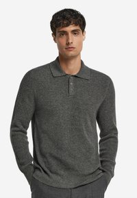 Grå ribbad tröja med långa ärmar, krage och knäppning med tre knappar. Tillverkad av strukturerat tyg med en åtsittande design.