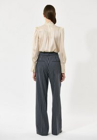 Bežna satinasta bluzica z nabrano ovratnikom in dolgimi, napihnjenimi rokavi, v kombinaciji z mornarsko modrimi hlačami širokega kroja s črtami in visokim pasom.