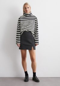 Maglione a righe a maniche lunghe con collo a imbuto in bianco e nero, abbinato a una gonna mini nera con spacco laterale. Le scarpe nere slip-on completano il look.