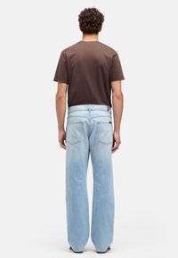 Jasnoniebieskie dżinsy o luźnym kroju, zestawione z brązowym T-shirtem. Dżinsy mają tylne kieszenie i prostą nogawkę.
