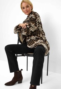 Cappotto di pelliccia sintetica con motivo a zigzag in crema, marrone e nero, indossato sopra pantaloni neri. Stivaletti in suede marrone con tacco a blocco.