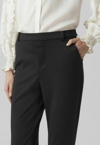 Svarta skräddarsydda byxor med en slät yta, med en framficka och slim fit, tillsammans med en vit blus med spetsdetaljer.