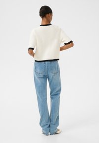 Cream short-sleeve sweater with black trim, paired with light blue wide-leg jeans. Soft texture, relaxed fit, visible back pockets on jeans.