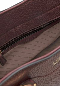 Interno di una borsa in pelle bordeaux, con rivestimento testurizzato, tasca con zip e un delicato motivo con logo su uno sfondo crema liscio.