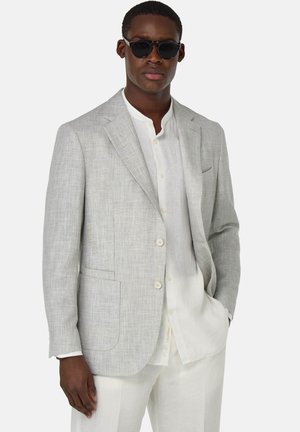 Blazer di lino grigio chiaro con finitura testurizzata, due bottoni, revers a lancia e tasche laterali, indossato sopra una camicia bianca e pantaloni chiari.