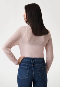 Lichtroze, aansluitende trui met lange mouwen en een doorschijnende rug. Draag het met high-waisted donkerblauwe denim jeans met twee achterzakken.