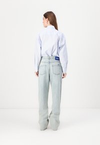 Camisa de rayas azul claro de corte oversize con puños de botón, combinada con jeans rectos azul pálido que presentan bolsillos traseros y una etiqueta de logo.
