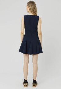 Robe sans manches bleu marine avec une silhouette ajustée évasée, présentant des plis au niveau de la jupe et une fermeture éclair au dos.