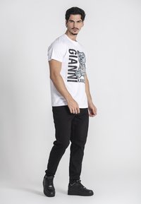 Camiseta blanca de algodón con un gráfico de un oso y texto en negro, combinada con unos vaqueros negros ajustados y zapatillas negras. Diseño simple, estilo casual.