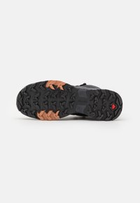Suola di scarpa da trail running nera con grip a motivo, dotata di audaci accenti arancioni e rossi. Materiale in gomma con superficie testurizzata.
