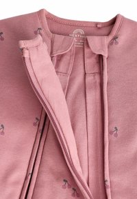 Ružičasta zip-up odjeća s printom trešnje. Ima mekan, pleteni tekstur i okrugli izrez. Uključuje prednji patentni zatvarač i detalj s kopčanjem na dugme.