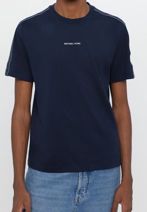 T-shirt di cotone blu navy con girocollo, maniche corte, testo bianco del brand "MICHAEL KORS" sul petto e cuciture a contrasto sulle spalle.