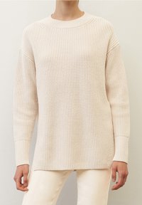Maglione lavorato a maglia beige chiaro con scollatura rotonda, spalle cadenti e maniche lunghe. Presenta una texture a coste e spacchi laterali all'orlo.