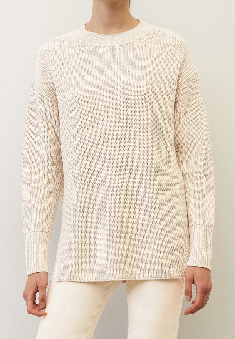 Maglione lavorato a maglia beige chiaro con scollatura rotonda, spalle cadenti e maniche lunghe. Presenta una texture a coste e spacchi laterali all'orlo.