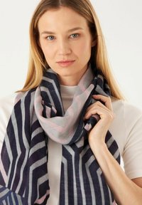 Écharpe tricotée avec des motifs zigzag bleu marine, gris et rose, texture douce et design drapé. Portée autour du cou.