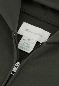Dunkelgrüne, weich gewebte Zip-Hoodie mit silbernem Reißverschluss. Etiketten zeigen "Champion" und Größe "Small." Glatte Textur, keine Muster.