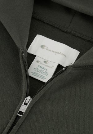 Felpa con zip di colore verde scuro, realizzata in tessuto morbido con una cerniera argento. Etichette mostrano "Champion" e taglia "Small." Tessuto liscio, senza motivi.