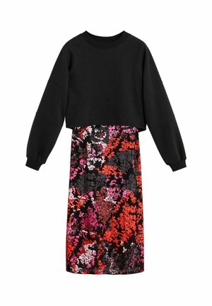 Zwarte cropped sweater met lange mouwen, gecombineerd met een midilengte rok met een abstracte bloemenprint in rood, roze en zwart.
