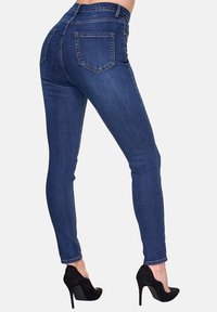 Dunkelblaue Skinny-Jeans aus Denim mit hohem Bund, zwei Gesäßtaschen und schlankem Schnitt. Kombiniert mit schwarzen High Heels.