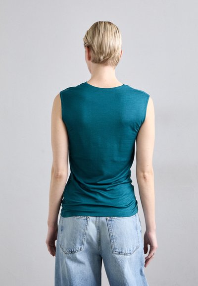 Teal ermeløs topp med rund hals, teksturert stoff og tettsittende design, sammen med lyseblå løse jeans.