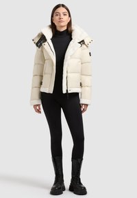 Cream puffer jacket with fur-lined collar, snap buttons, and adjustable straps. Paired with black leggings and combat boots.