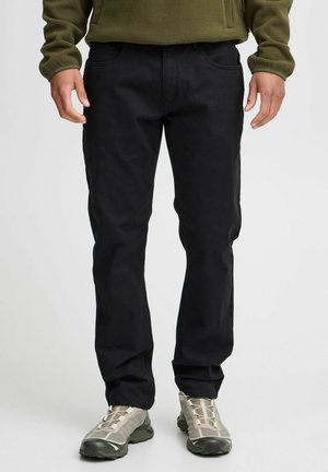 Black cotton trousers with a classic cut, front pockets, and subtle texture. Paired with light gray hiking shoes for contrast.
