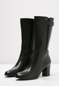 Black leather knee-high boots with a pointed toe and block heel, featuring a side zipper and strap detail at the top. Smooth texture.