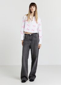 White cropped blouse with pink bow accents, paired with high-waisted, loose-fitting gray jeans. Simple, minimalist backdrop.