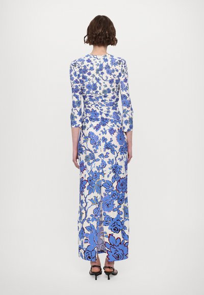 Long dress in white with blue floral pattern, fitted bodice, three-quarter sleeves, and back slit. Smooth fabric with slight sheen.