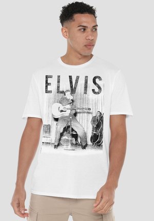 Mann trägt weißes T-Shirt mit schwarz-weißem Bild von Elvis Presley, der auf der Bühne Gitarre spielt, mit dem Schriftzug "ELVIS" darüber.