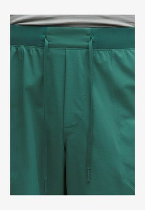 Zaļas teksturētas sporta bikses ar elastīgu vidukļa jostu, divām priekšējām kabatām un aukliņām, kas karājas centrā.