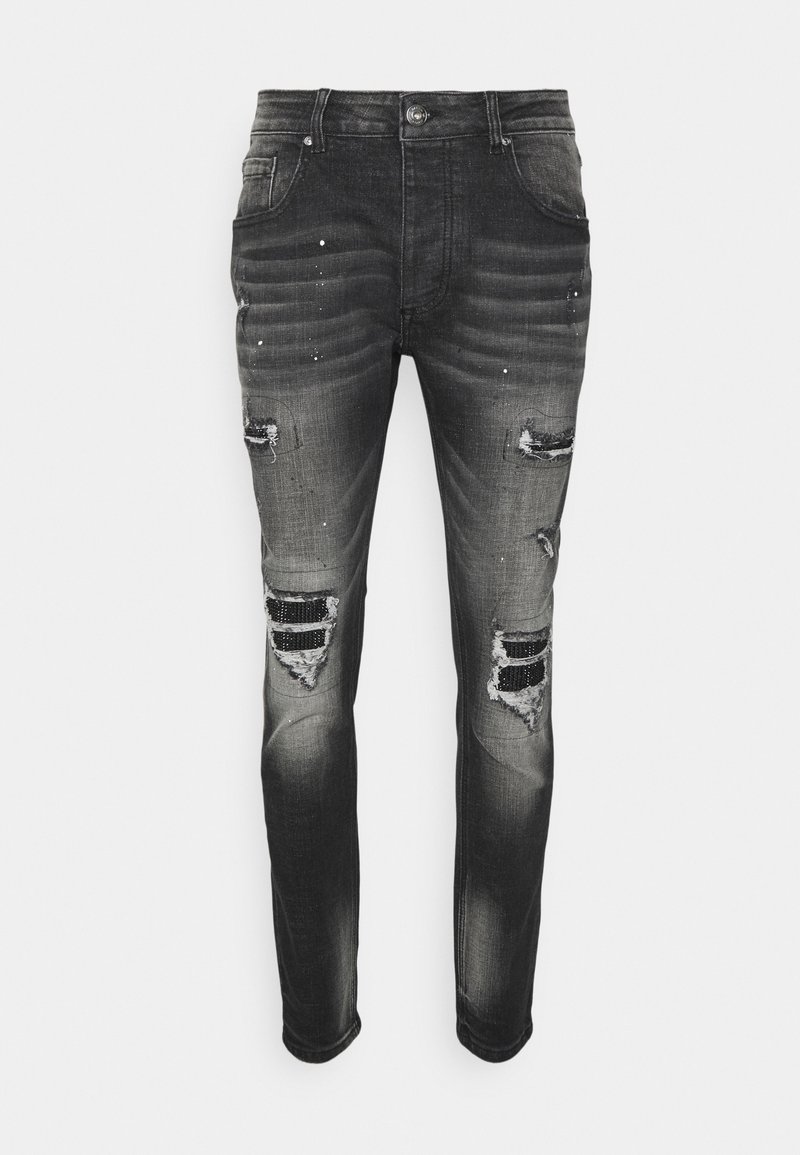 Jean en denim noir avec des zones délavées, des déchirures usées et des éclaboussures de peinture. Présente une coupe slim et un design classique à cinq poches.
