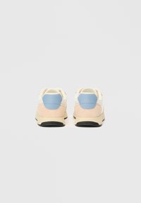 Ζευγάρι μπεζ και λευκών αθλητικών παπουτσιών με μπλε πίσω τμήματα και μαύρες σόλες, απεικονισμένα από πίσω σε λευκό φόντο.