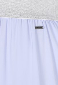 Vaaleansininen mekko, jossa on teksturoitu hopeinen yläosa ja valuva hame. Siinä on pieni metallilappu, jossa lukee "DREIMASTER".