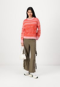 Knit sweater in red and pink stripes with textured pattern; paired with khaki cargo pants featuring side pockets; white handbag and sneakers.