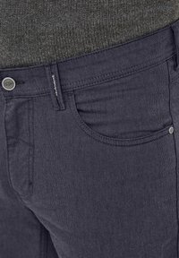 Dunkel marineblaue Hose aus strukturiertem Stoff, mit Knopfverschluss und Fünf-Taschen-Design sowie sichtbaren Nahtdetails.