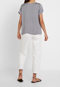 Top gris de manga corta con cuello redondo y dobladillo curvado, combinado con pantalones cortos blancos y sandalias planas negras.