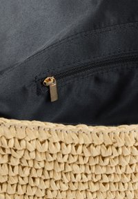 Intérieur en tissu noir avec une poche zippée dorée fermée à l'intérieur d'un bord de sac en paille tissée visible en bas.
