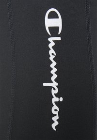 Czarne legginsy sportowe o dopasowanym kroju, z białym nadrukiem logo "Champion". Gładka faktura i kontrastujące detale szwów.