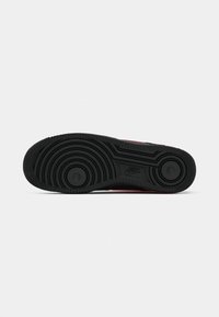 Nike sneaker outsole in black, featuring a wavy tread pattern with circular accents and textured edges for grip and durability.