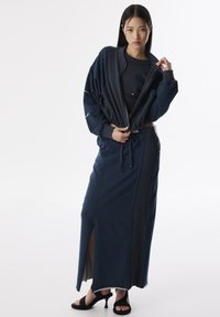 Marineblauw sportset bestaande uit een cropped ritsjack en een rok met hoge split. Zachte textuur, relaxte pasvorm en details met een trekkoord in de taille.